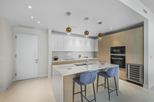 kitchen featuring oven, sink, an island with sink, decorative light fixtures, and white cabinetry