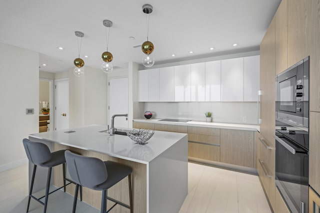 kitchen with pendant lighting, a kitchen island with sink, white cabinets, black appliances, and light brown cabinetry