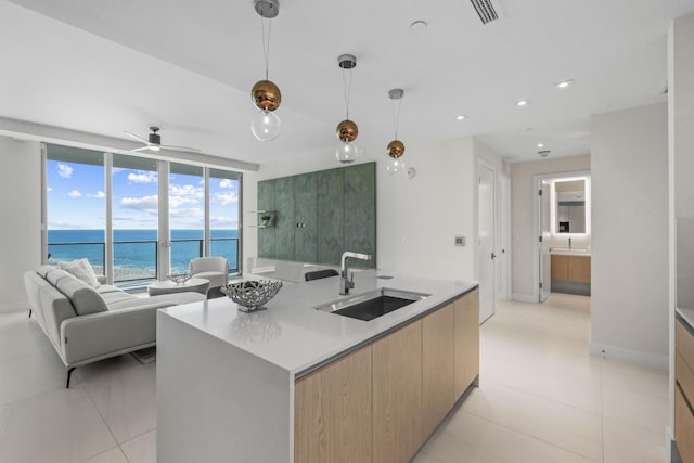 kitchen featuring ceiling fan, a kitchen island with sink, sink, a water view, and hanging light fixtures