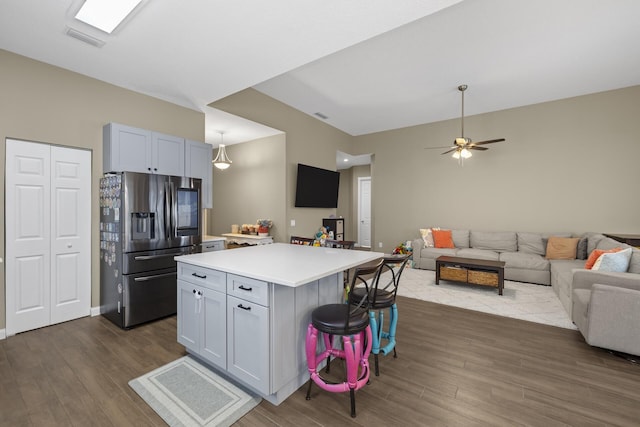 kitchen with ceiling fan, a kitchen breakfast bar, stainless steel fridge with ice dispenser, dark hardwood / wood-style flooring, and a kitchen island