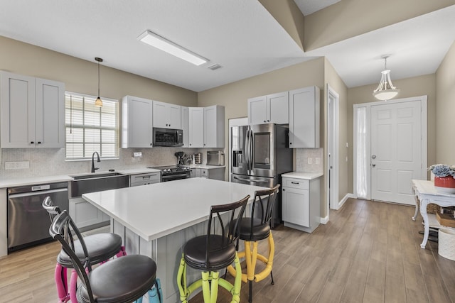 kitchen with a center island, sink, light hardwood / wood-style flooring, appliances with stainless steel finishes, and decorative light fixtures