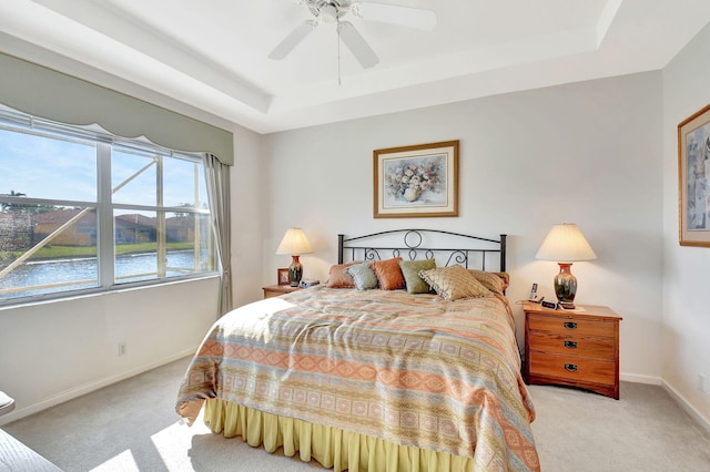 carpeted bedroom with ceiling fan, a water view, and a tray ceiling