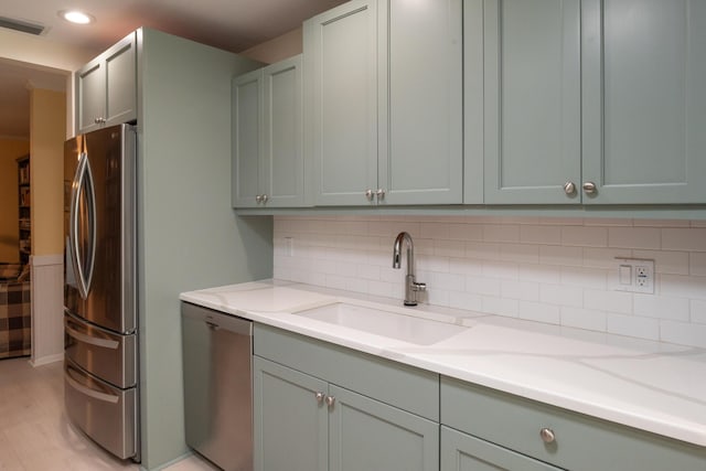 kitchen with light stone counters, tasteful backsplash, light wood-type flooring, appliances with stainless steel finishes, and sink