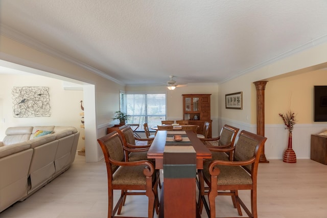 dining space featuring ornamental molding, ceiling fan, a textured ceiling, light hardwood / wood-style flooring, and decorative columns