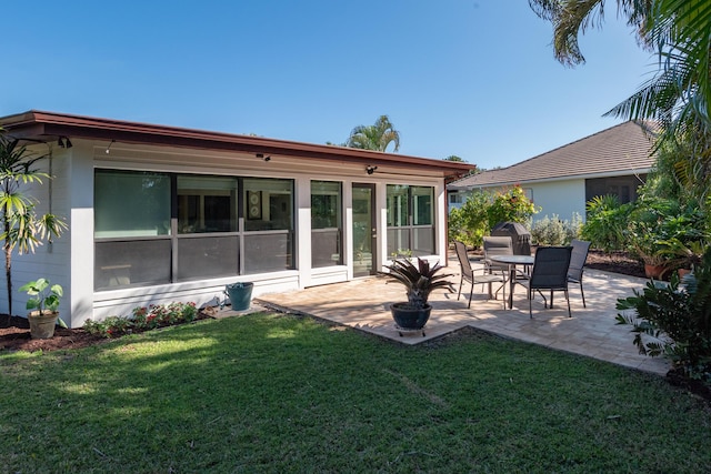 rear view of property featuring a lawn, a sunroom, and a patio area