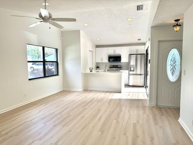 kitchen with stainless steel appliances, white cabinetry, a textured ceiling, light wood-type flooring, and decorative backsplash