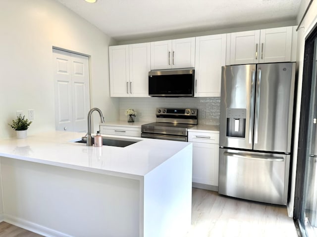 kitchen with stainless steel appliances, kitchen peninsula, sink, white cabinetry, and tasteful backsplash