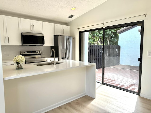 kitchen with stainless steel appliances, sink, white cabinetry, vaulted ceiling, and light hardwood / wood-style floors