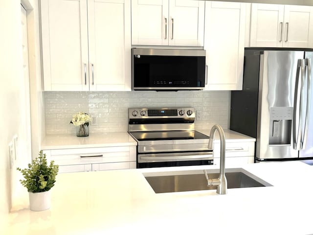 kitchen featuring appliances with stainless steel finishes, white cabinetry, decorative backsplash, and sink