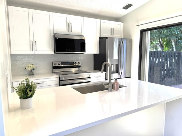 kitchen with a textured ceiling, stainless steel appliances, backsplash, white cabinets, and sink