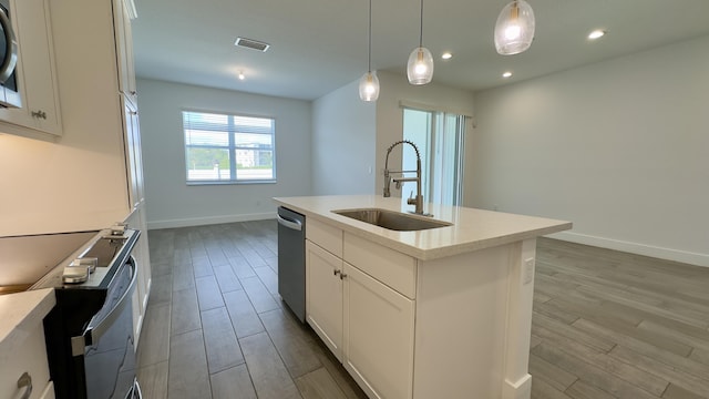 kitchen featuring sink, dishwasher, hanging light fixtures, white cabinets, and a center island with sink