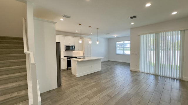 kitchen featuring appliances with stainless steel finishes, decorative light fixtures, white cabinetry, decorative backsplash, and a center island with sink