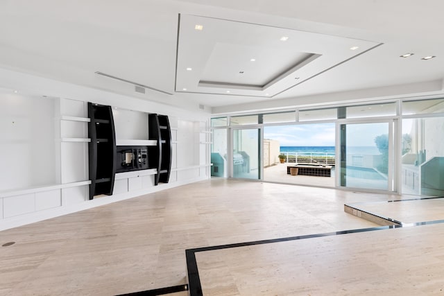 unfurnished living room featuring a tray ceiling, a water view, and a wall of windows