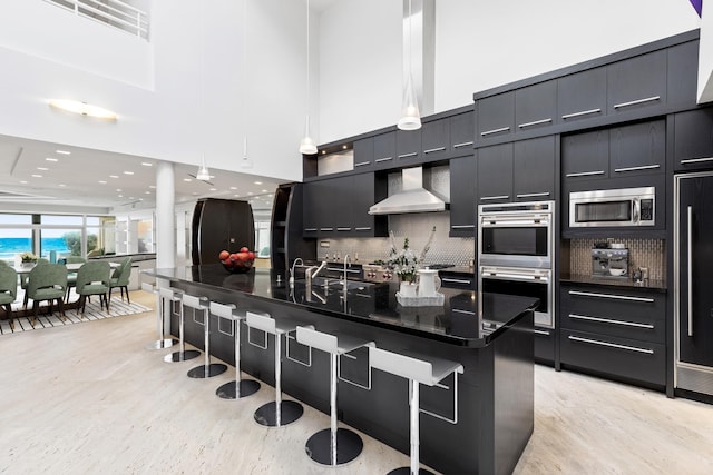 kitchen with a center island with sink, wall chimney exhaust hood, a kitchen bar, and stainless steel appliances