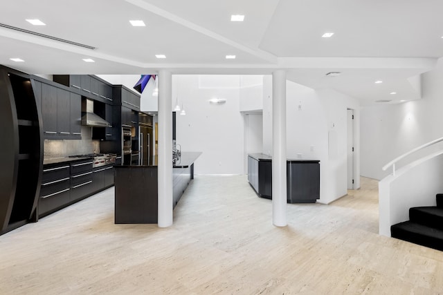 kitchen featuring a kitchen island, light wood-type flooring, wall chimney range hood, and tasteful backsplash