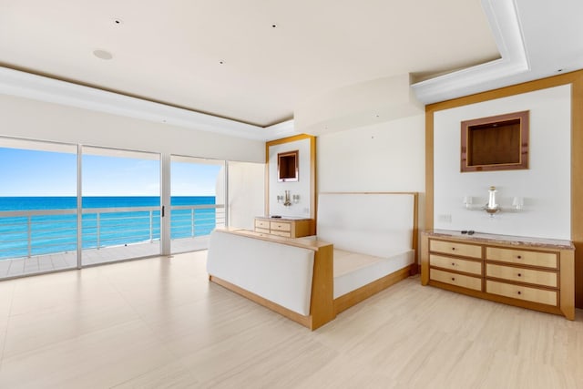 unfurnished bedroom featuring access to outside, a raised ceiling, and a water view