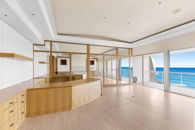 kitchen with kitchen peninsula, expansive windows, a raised ceiling, light brown cabinets, and a water view