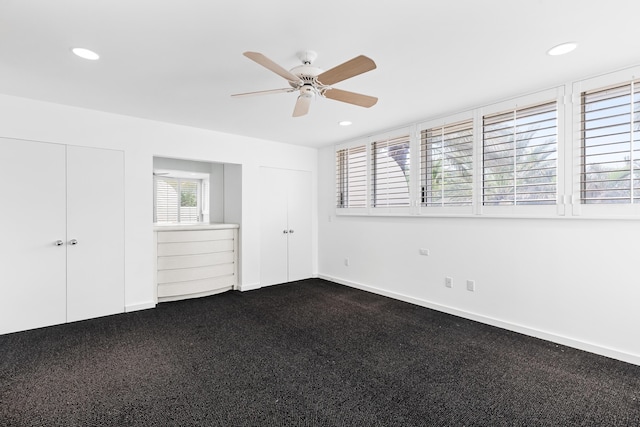 unfurnished bedroom with ceiling fan and dark colored carpet