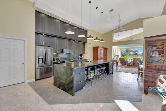 kitchen featuring appliances with stainless steel finishes, a breakfast bar, hanging light fixtures, a kitchen island with sink, and ceiling fan