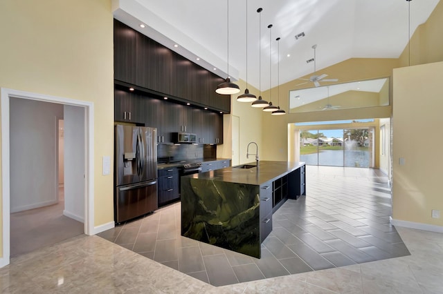 kitchen featuring stainless steel appliances, dark countertops, hanging light fixtures, a kitchen island with sink, and dark brown cabinets