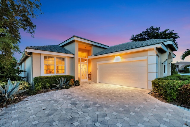 view of front of home featuring a garage, a tiled roof, decorative driveway, and stucco siding