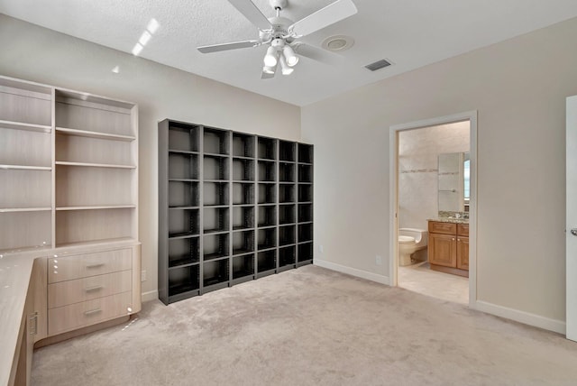 unfurnished bedroom featuring light carpet, connected bathroom, a textured ceiling, and ceiling fan