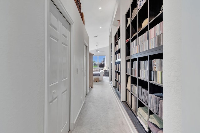 hallway featuring recessed lighting, light colored carpet, a textured wall, and baseboards