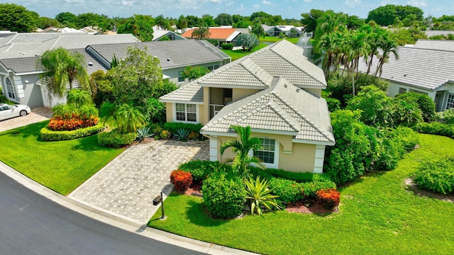 view of front of house featuring a tiled roof, decorative driveway, a residential view, stucco siding, and a front lawn