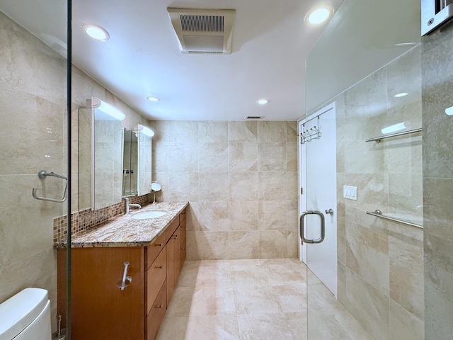 bathroom with vanity, a shower with shower door, tile walls, and toilet