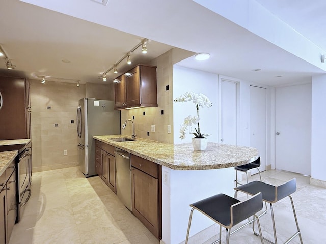 kitchen with sink, stainless steel appliances, light stone counters, a kitchen bar, and decorative backsplash