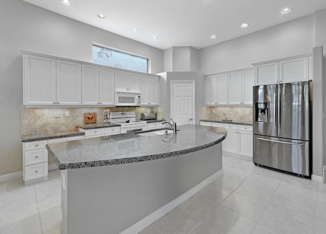 kitchen featuring sink, dark stone counters, white appliances, a center island with sink, and light tile patterned floors