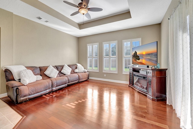 living room featuring ceiling fan, light hardwood / wood-style flooring, and a tray ceiling