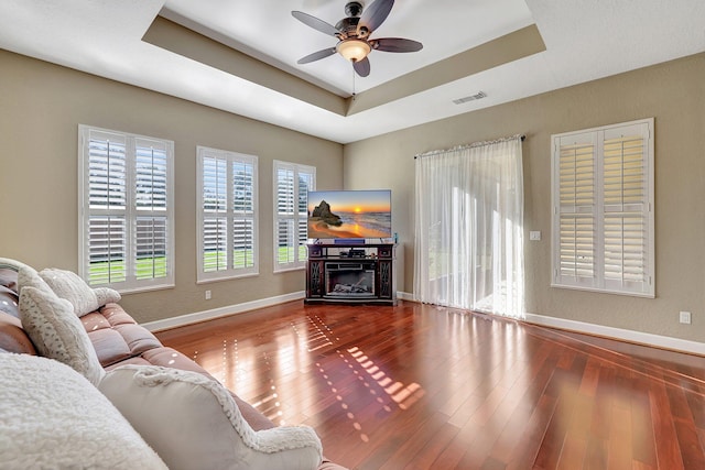 living room with hardwood / wood-style flooring, a raised ceiling, and ceiling fan