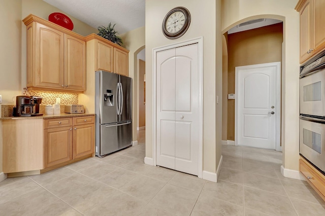 kitchen with light stone countertops, light brown cabinets, backsplash, light tile patterned flooring, and appliances with stainless steel finishes