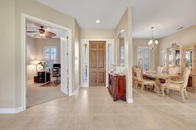 tiled foyer entrance with ceiling fan with notable chandelier and a wealth of natural light