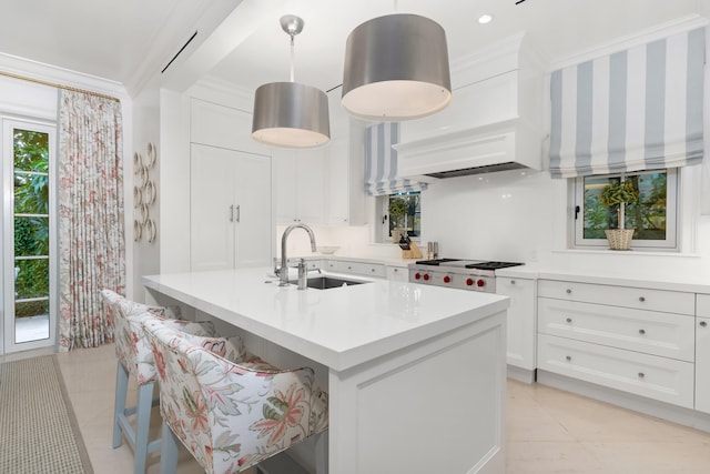 kitchen with a breakfast bar, a kitchen island with sink, sink, and white cabinets