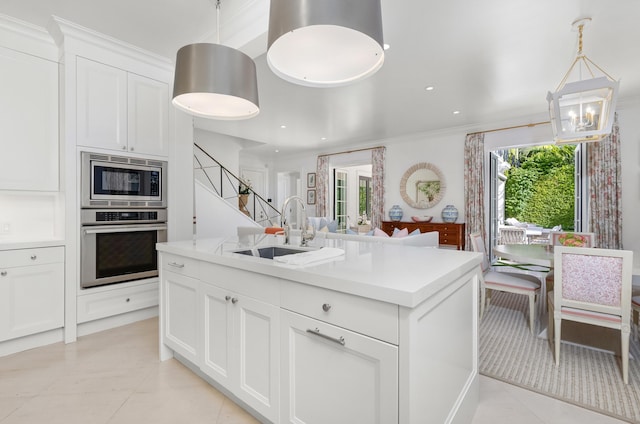 kitchen featuring appliances with stainless steel finishes, sink, pendant lighting, a center island with sink, and white cabinetry