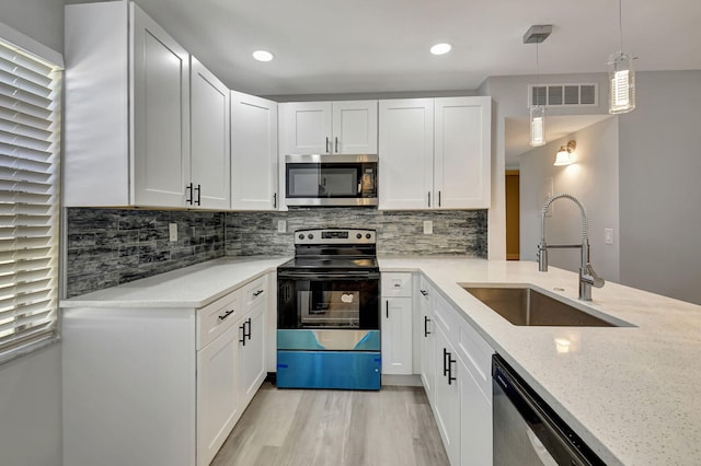 kitchen featuring light stone countertops, white cabinetry, sink, stainless steel appliances, and decorative light fixtures