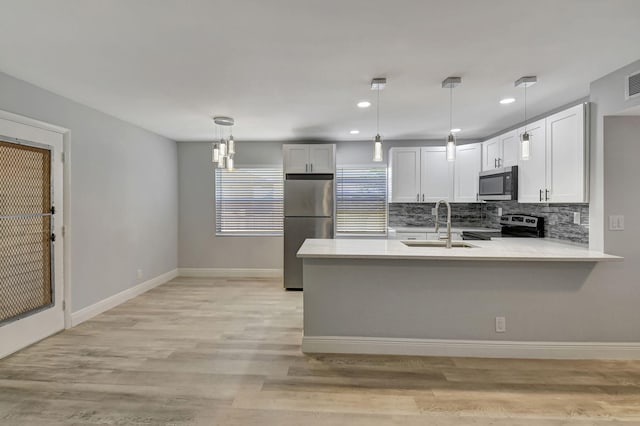 kitchen featuring kitchen peninsula, light wood-type flooring, stainless steel appliances, decorative light fixtures, and white cabinets