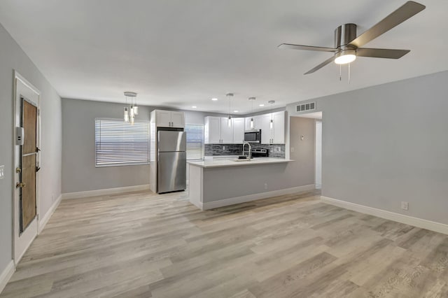 kitchen featuring kitchen peninsula, stainless steel appliances, pendant lighting, light hardwood / wood-style flooring, and white cabinetry