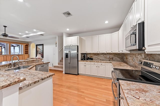 kitchen featuring sink, white cabinets, stainless steel appliances, light stone countertops, and light hardwood / wood-style flooring