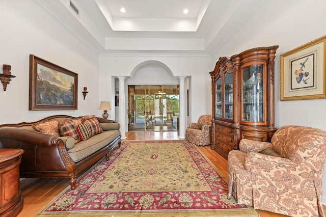 living room featuring a tray ceiling, decorative columns, and light hardwood / wood-style flooring