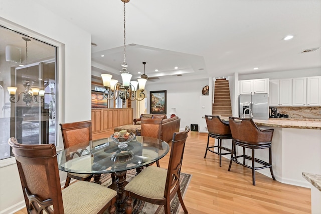 dining area featuring an inviting chandelier, a tray ceiling, and light hardwood / wood-style floors