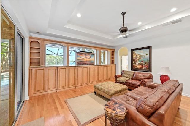 living room with light hardwood / wood-style flooring, a raised ceiling, and ceiling fan