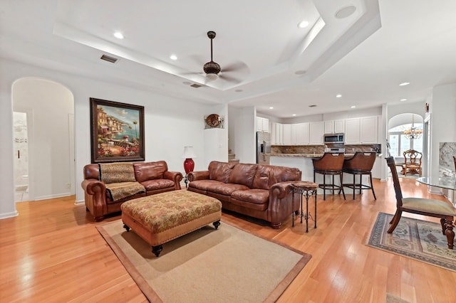 living room with a tray ceiling, light hardwood / wood-style flooring, and ceiling fan with notable chandelier