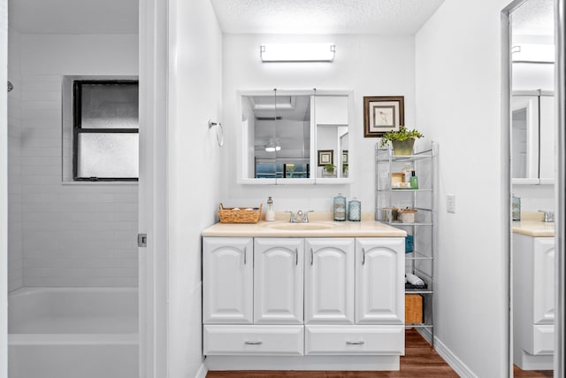 bathroom featuring a textured ceiling, tiled shower / bath combo, wood-type flooring, and vanity