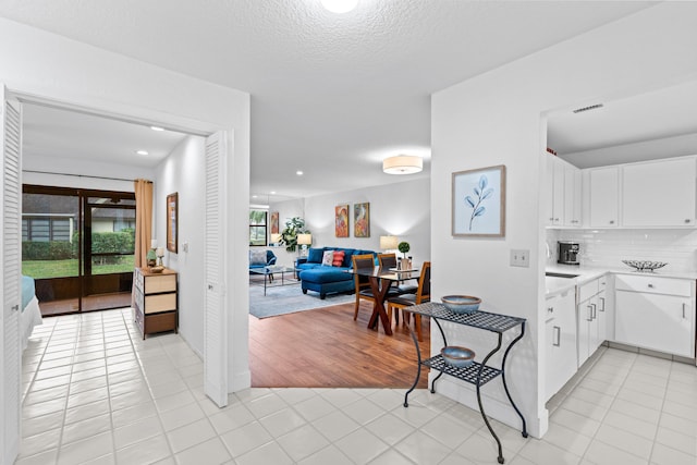 kitchen with tasteful backsplash, light tile patterned flooring, white cabinetry, and a textured ceiling