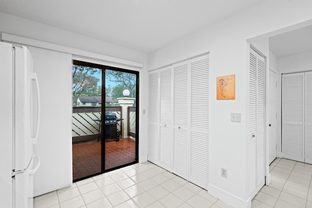 unfurnished bedroom featuring light tile patterned floors, multiple closets, white refrigerator, and access to outside