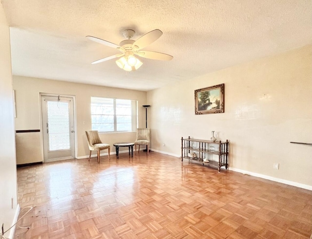 living area with ceiling fan, light parquet floors, and a textured ceiling