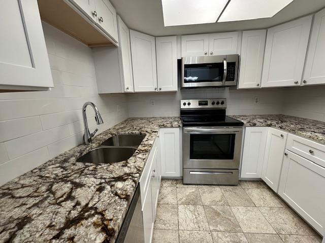 kitchen with white cabinets, stainless steel appliances, light stone countertops, and sink